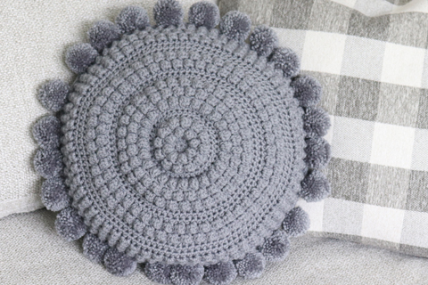 round crochet pillow with yarn pom pom around edge